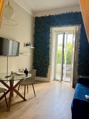 Ein Zimmer mit Esstisch, Stühlen, einem Fernseher, einem blauen Sofa und einer Glastür, die zu einem Außenbereich führt.