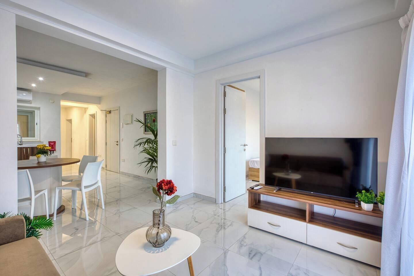 A modern living room with a flat-screen TV, a coffee table, and a dining area with chairs.