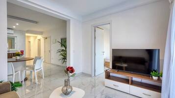 A modern living room with a flat-screen TV, a coffee table, and a dining area with chairs.