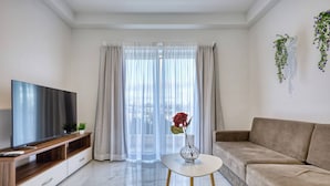 Un salon moderne avec un téléviseur à écran plat, un canapé, une table basse agrémentée d’un vase et des rideaux légers.