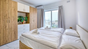 Une chambre d’hôtel avec un lit, une armoire en bois, une plante en pot et une fenêtre avec des rideaux.