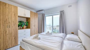 Hotellihuone, jossa on sänky, puinen vaatekaappi, ruukussa oleva kasvi ja ikkuna, jossa on verhot.