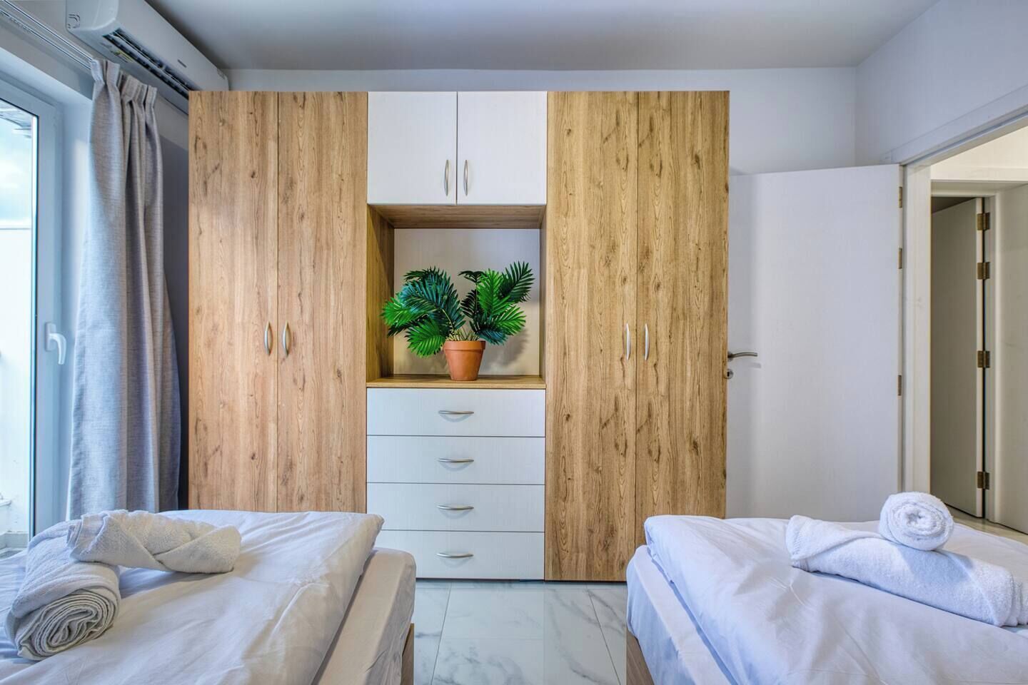 A hotel room with two beds, a wardrobe with a plant, and a bathroom door.