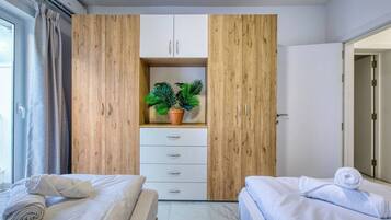 A hotel room with two beds, a wardrobe with a plant, and a bathroom door.