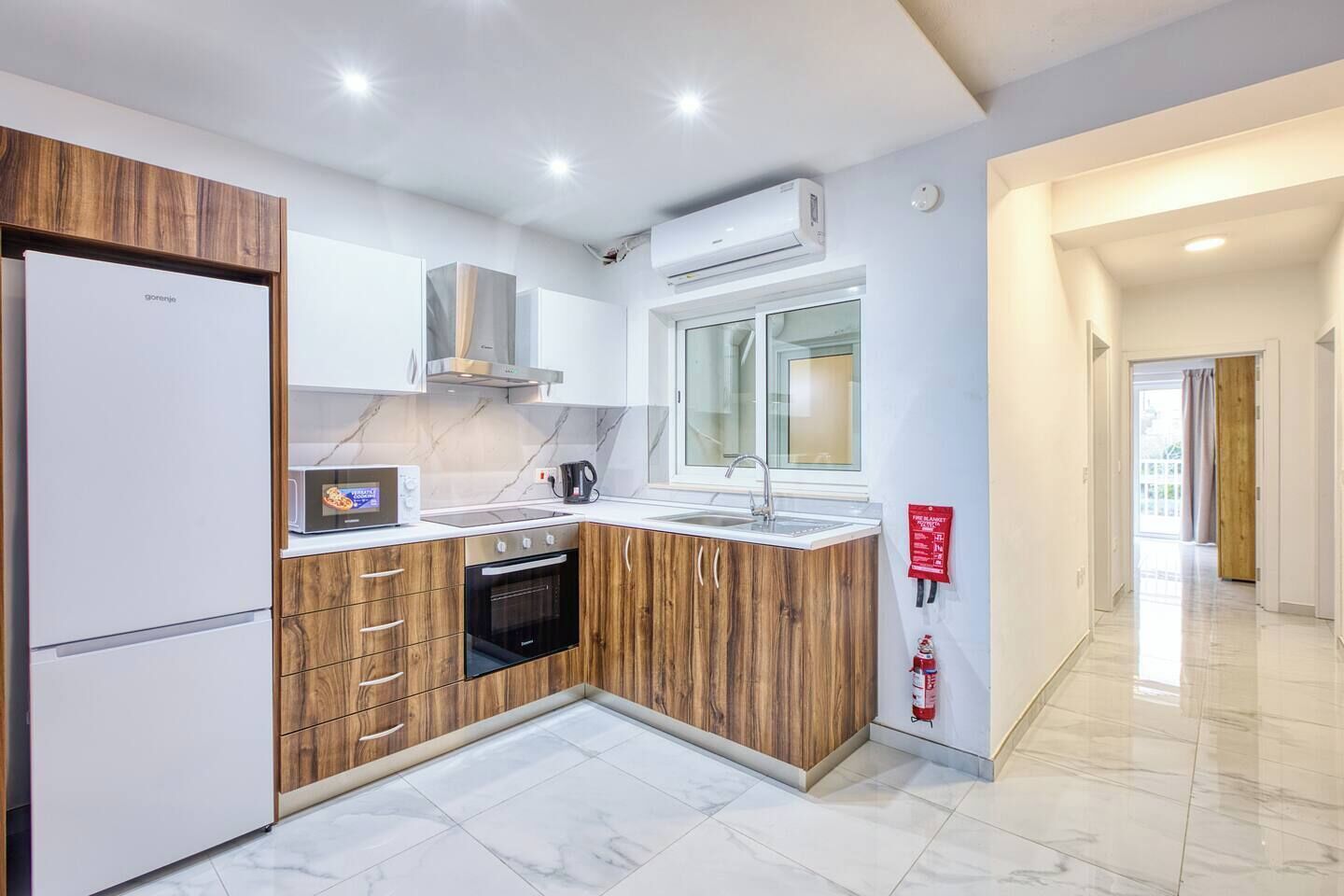 A modern kitchen with a built-in oven, microwave, and a window above the sink.