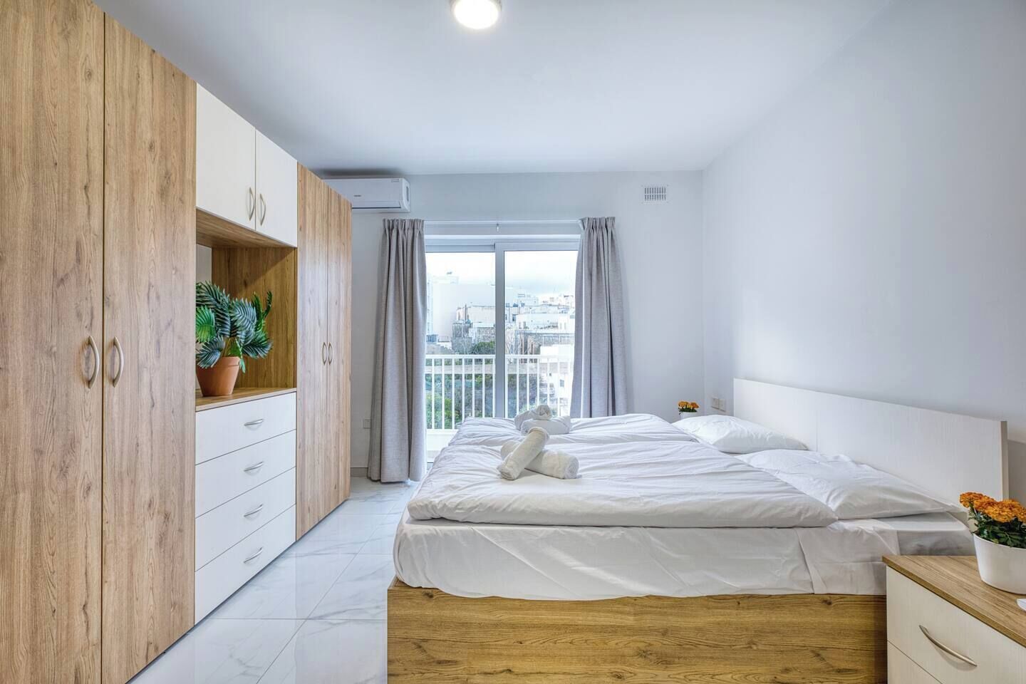 A bedroom with a bed, wooden wardrobe, and a balcony with a city view.