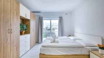 A bedroom with a bed, wooden wardrobe, and a balcony with a city view.