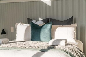 A neatly made bed with a white comforter, a teal accent pillow, and a white towel on the side.