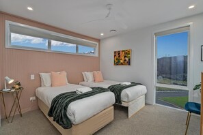 A bedroom with two beds, a window, and a view of a landscape. - Rings Beach Retreat - Award Winning Home (Kūaotunu West)