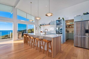 A modern kitchen with a large island, bar stools, stainless steel appliances, and a view of the ocean.
