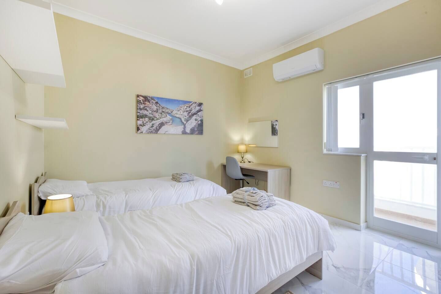 Une chambre d’hôtel avec deux lits, un bureau, une chaise, une lampe et un tableau au mur.