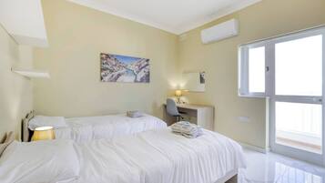 A hotel room with two beds, a desk, a chair, a lamp, and a painting on the wall.
