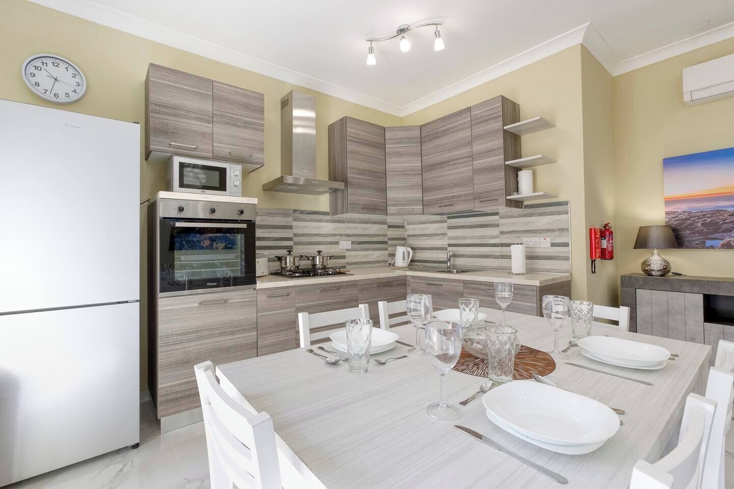 Une cuisine moderne équipée d’un four encastré, d’un four à micro-ondes et d’une cuisinière à gaz. On y trouve une table à manger mise avec des assiettes, des verres et des couverts.
