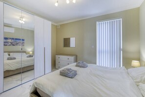 Ein Schlafzimmer mit Bett, Kleiderschrank, Kommode, Spiegel und einem Fenster mit Jalousien.