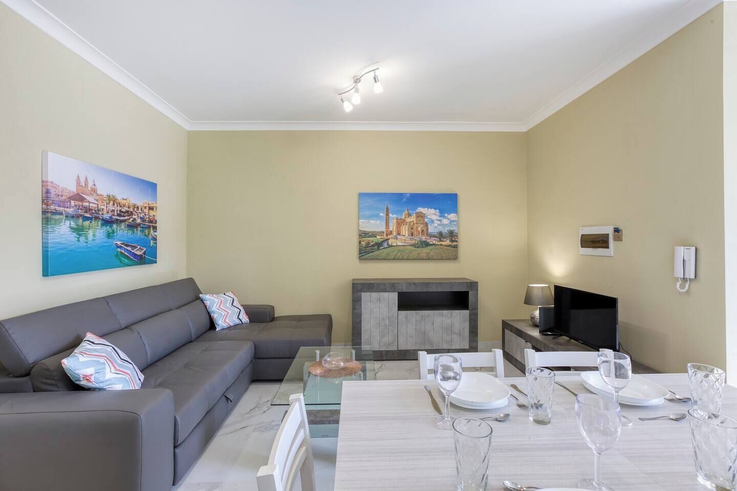 Un salon avec un canapé, une table à manger dressée pour quatre personnes et deux tableaux accrochés au mur.