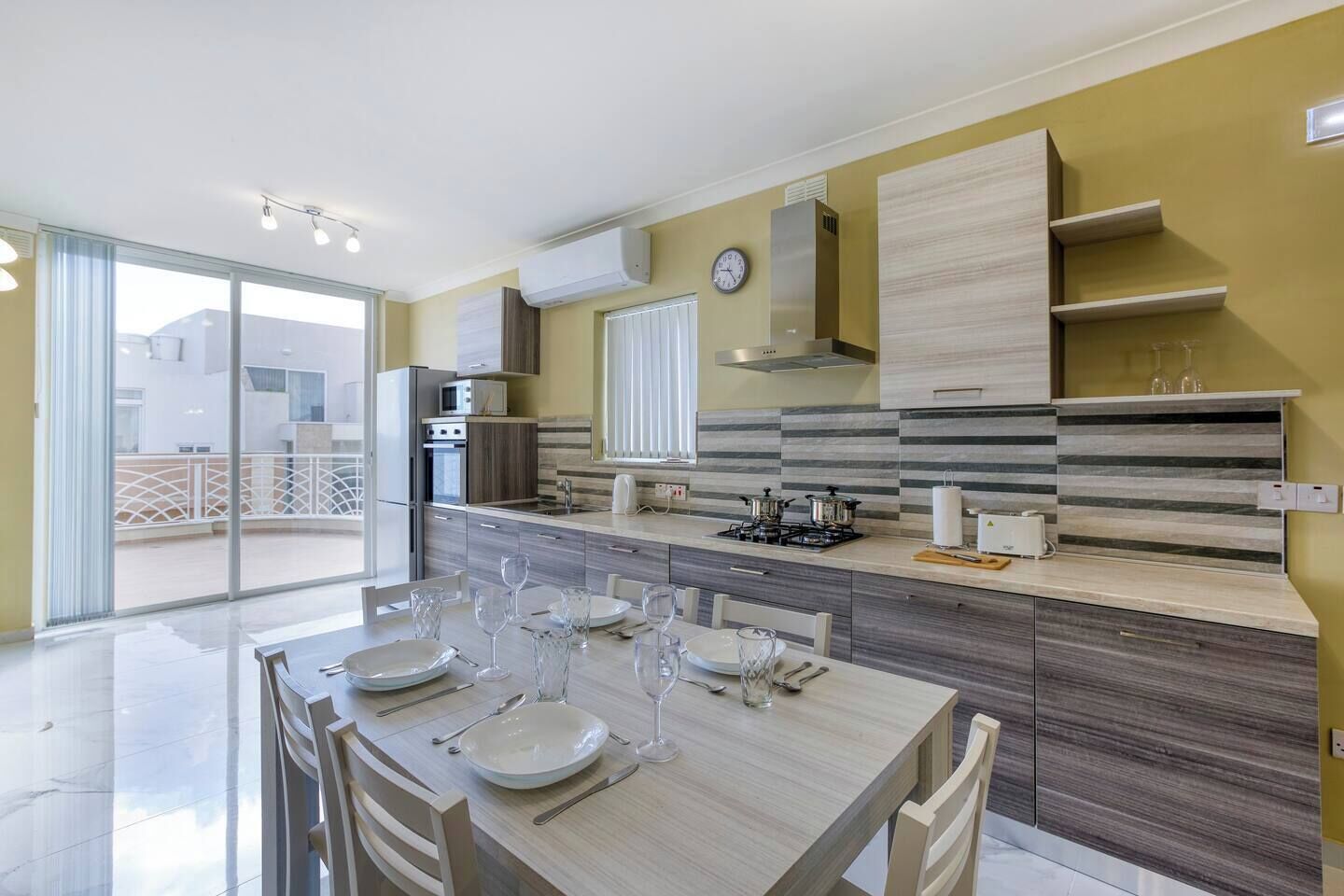Une cuisine moderne avec un coin repas, comprenant une grande table dressée pour six personnes, une cuisinière à gaz et un four encastré.