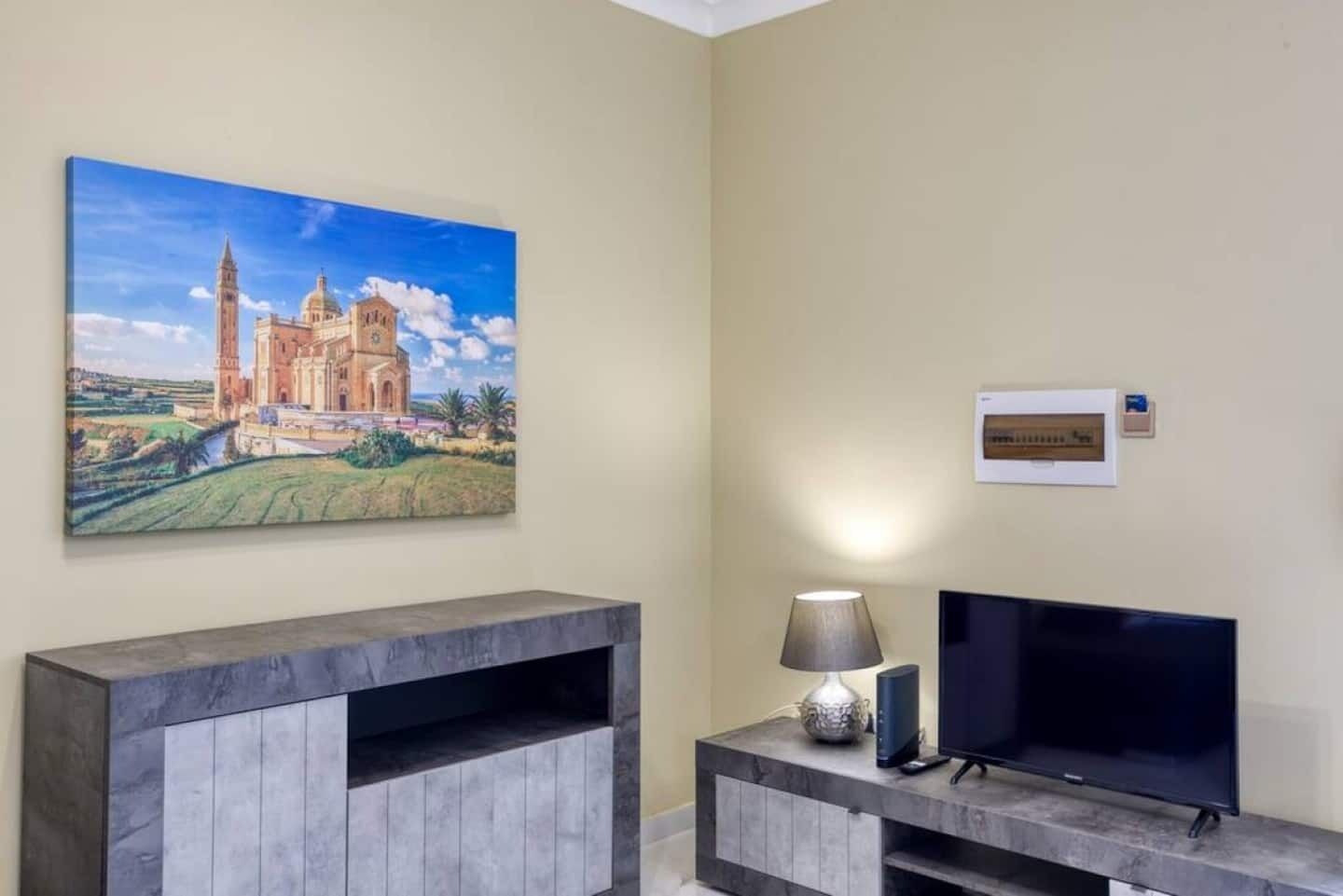 Une pièce comprenant un grand tableau représentant une cathédrale, un téléviseur à écran plat, une lampe et un certificat encadré accroché au mur.