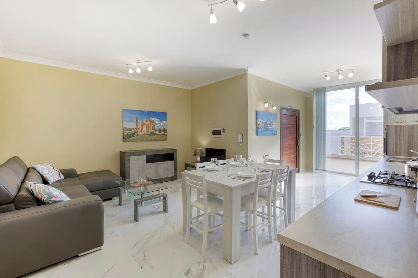 Un salon moderne avec un canapé, une table basse en verre et un coin repas comprenant une table et des chaises blanches.
