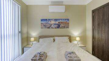 Una habitación de hotel con una cama, dos lámparas de noche, un cuadro en la pared y una puerta.