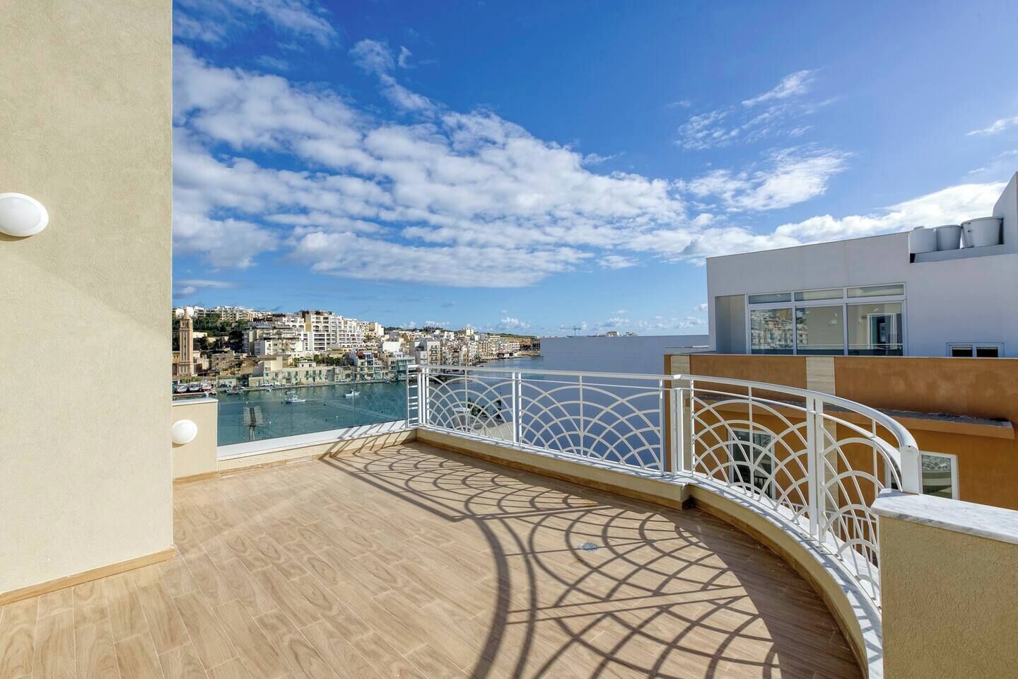 Un balcon offrant une vue sur un port de plaisance et des immeubles, avec un sol à motifs et une balustrade blanche.