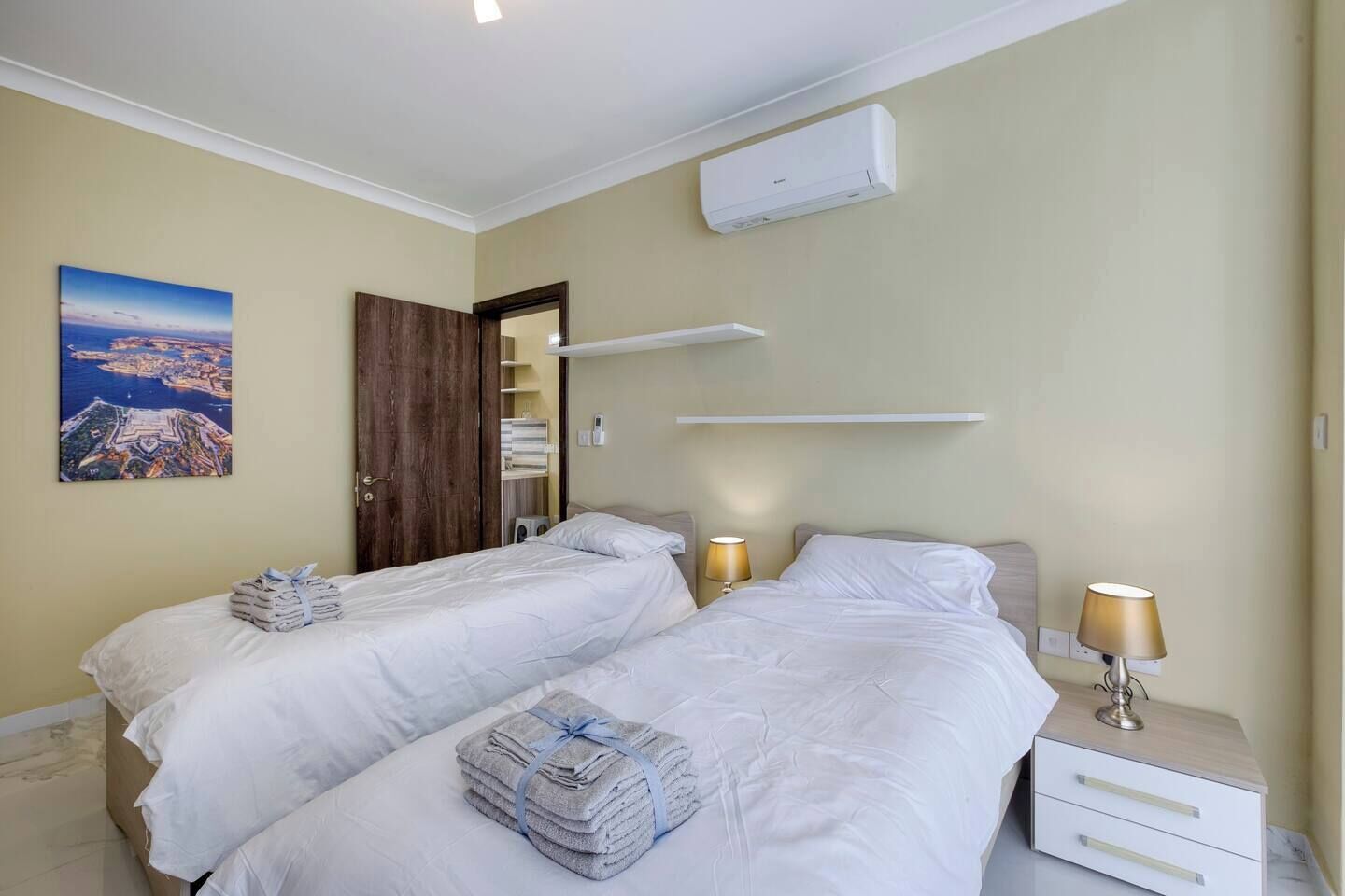 Une chambre d’hôtel avec deux lits, une armoire en bois, un tableau, un appareil de climatisation et des lampes de chevet.
