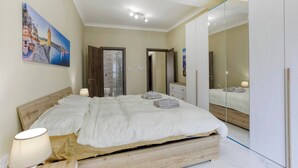 Ein Schlafzimmer mit Bett, Nachttischlampen, einem Holz-Kopfende, einer Duschkabine aus Glas, einem Kleiderschrank und einem Bild an der Wand.