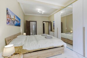 Une chambre à coucher avec un lit, des lampes de chevet, une tête de lit en bois, une cabine de douche en verre, une armoire et un tableau au mur.