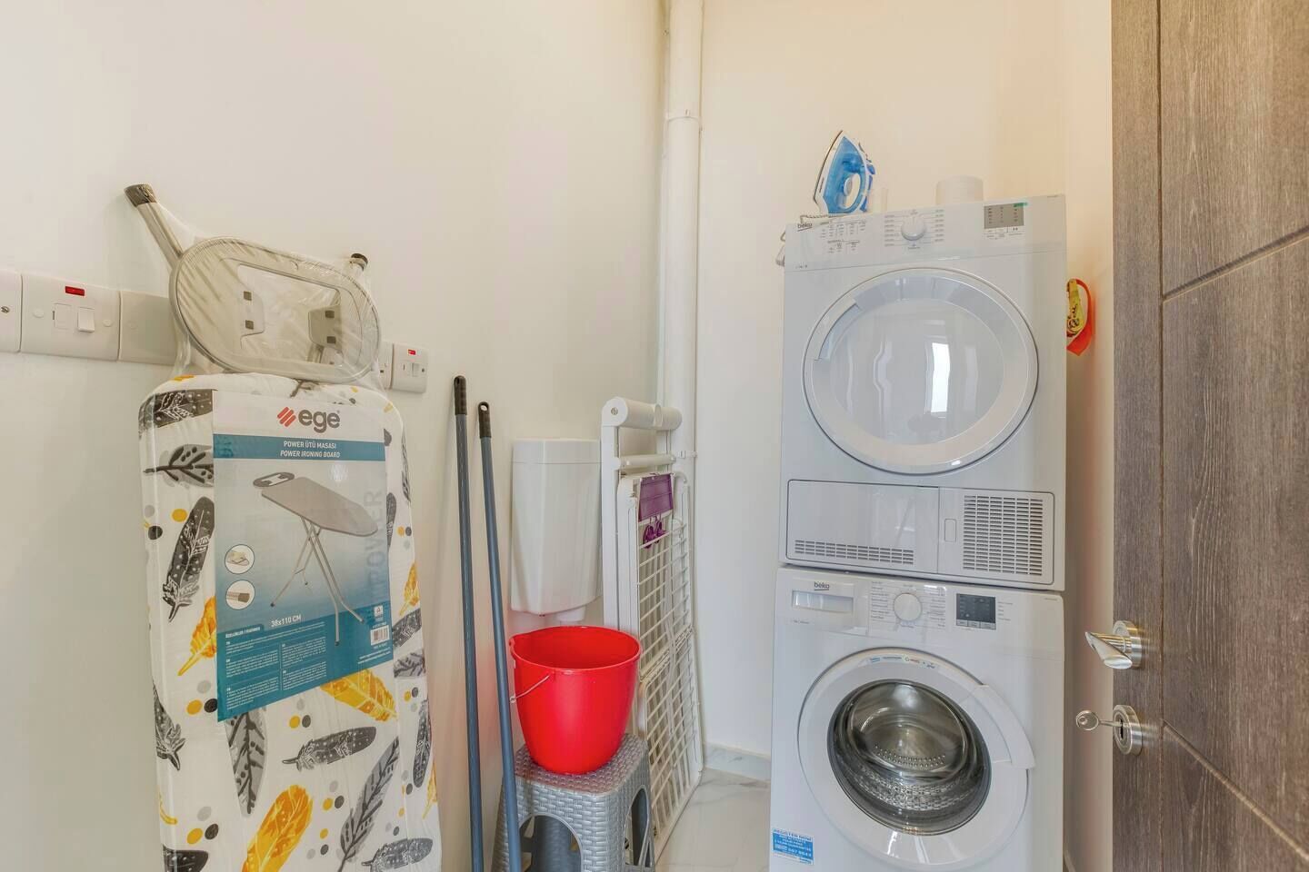 Un espace buanderie comprenant un lave-linge, un sèche-linge et un seau rouge.