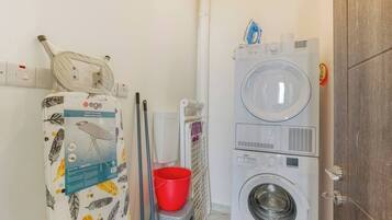 Un espace buanderie comprenant un lave-linge, un sèche-linge et un seau rouge.