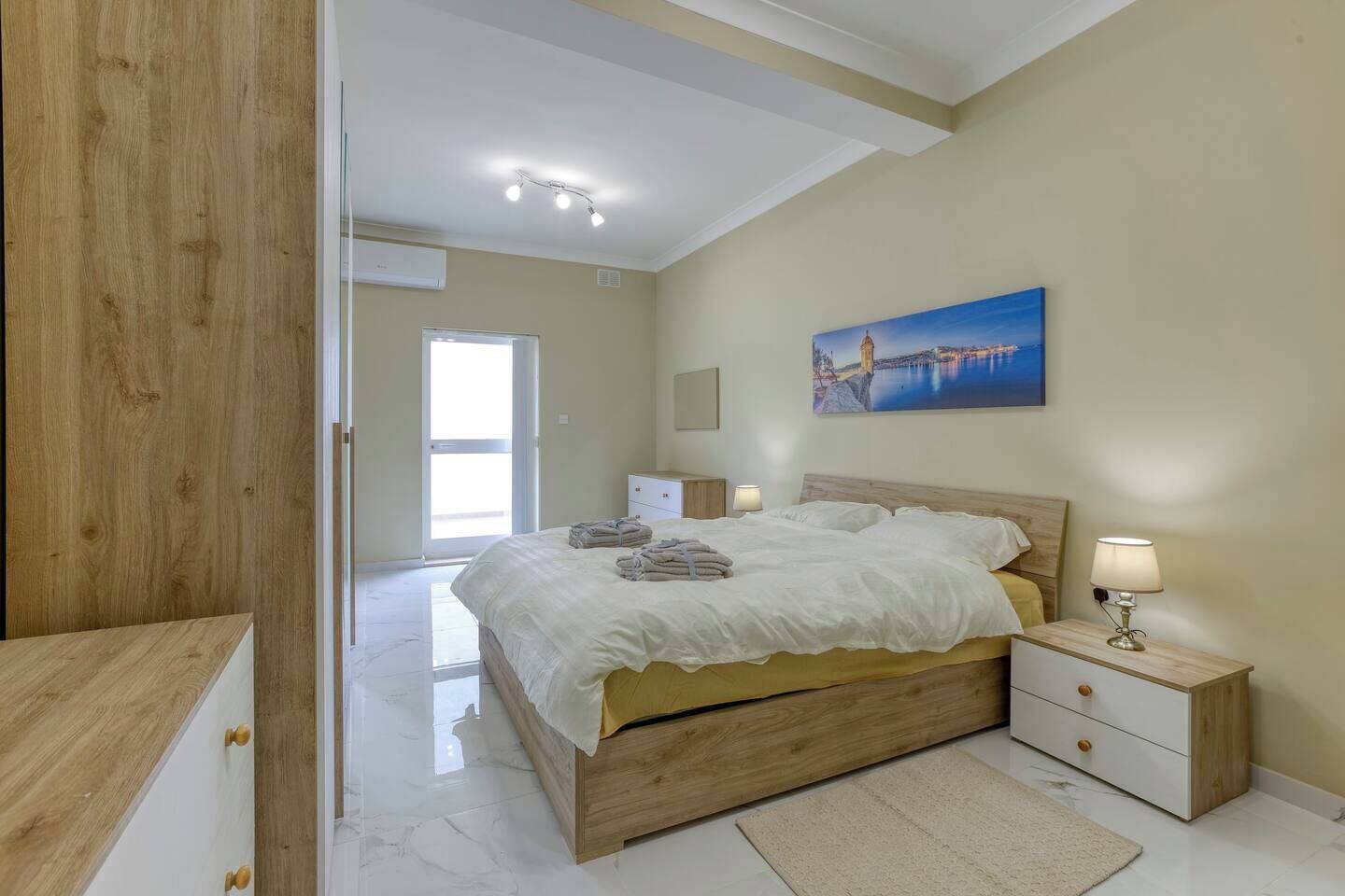 Une chambre à coucher avec un lit en bois, des tables de chevet, un tableau et une vue sur l’extérieur par une porte ouverte.