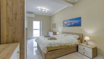 Une chambre à coucher avec un lit en bois, des tables de chevet, un tableau et une vue sur l’extérieur par une porte ouverte.