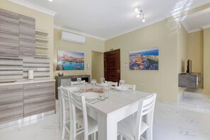 Un coin repas avec une table blanche dressée pour six personnes, un buffet en bois et deux tableaux accrochés au mur.