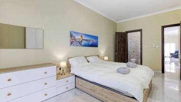 A bedroom with a bed, bedside tables, a mirror, a painting, and a door leading to another room.