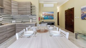 Un comedor moderno con una mesa de mármol, sillas blancas y una cocina con armarios grises.