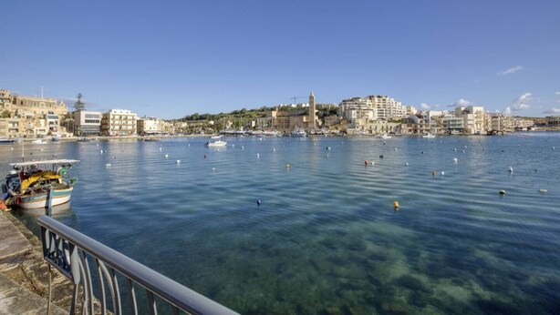 Un pueblo costero con un puerto deportivo, aguas azules cristalinas y edificios a lo largo de la costa.