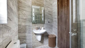 Un baño con pared de mármol, un lavamanos, un inodoro, un cubo de basura y una puerta de madera.