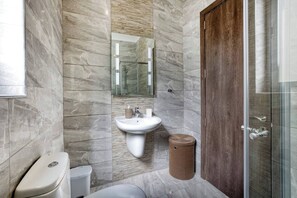 Un baño con pared de mármol, un lavamanos, un inodoro, un cubo de basura y una puerta de madera.