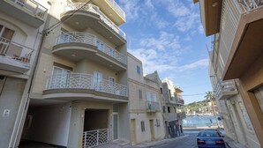 Un edificio residencial de varios pisos con balcones, una zona de estacionamiento y cielo despejado.