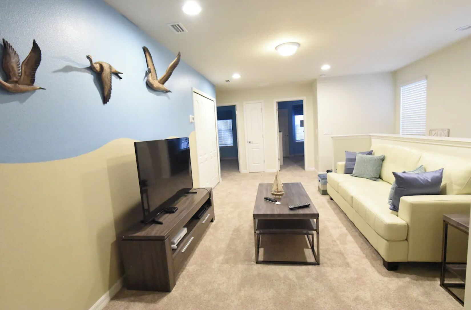 A living room with a flat-screen TV, a coffee table, a sofa, and wall-mounted bird decorations.
