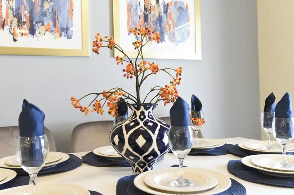 Et spisebord dækket med blå servietter, hvide tallerkener og en vase med orange blomster.