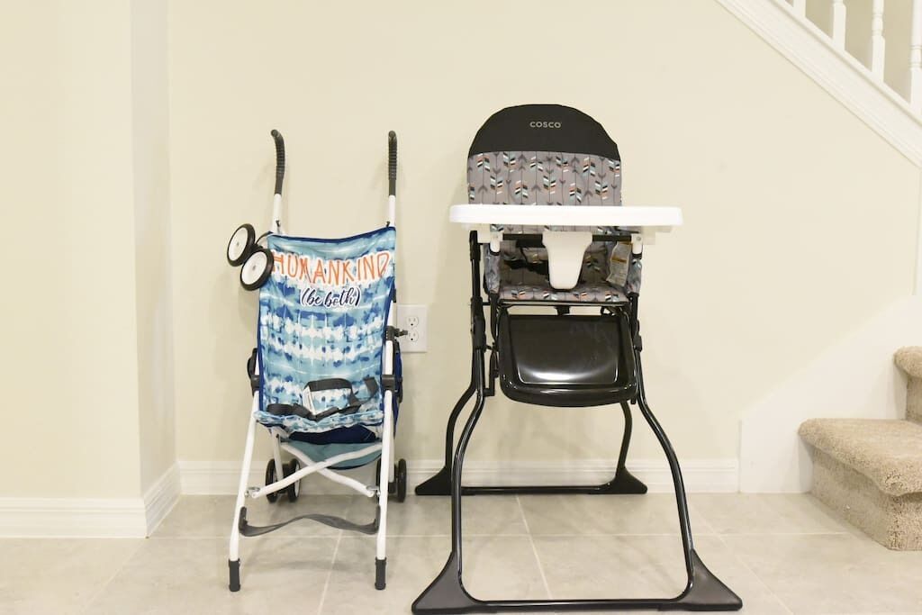 A baby stroller and a high chair in a room with a staircase.