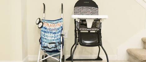 A baby stroller and a high chair in a room with a staircase.