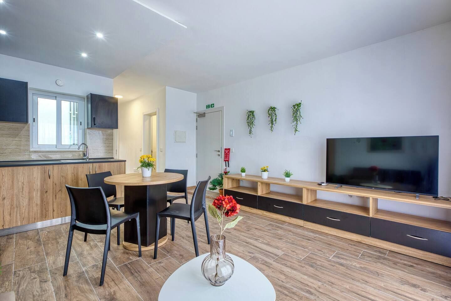 A modern kitchen with a dining area, a TV, and a plant wall.