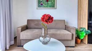 Un salon avec un canapé, un vase en verre rempli de fleurs et un tableau accroché au mur.