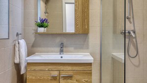 Une salle de bain avec un meuble-lavabo en bois, un miroir, un évier et une douche.