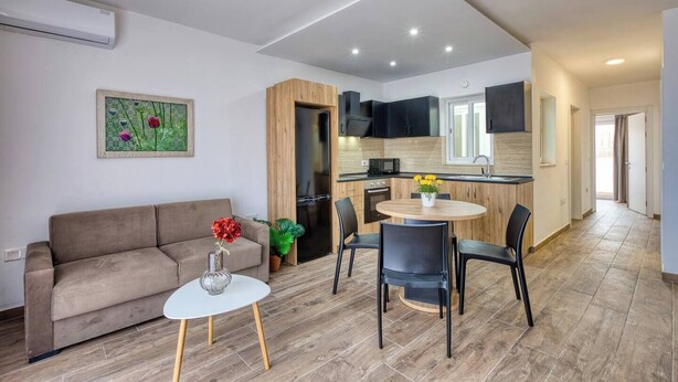 Un salon moderne avec un canapé, une petite table ronde et un coin repas avec des chaises. Il y a aussi une cuisine équipée d’un four à micro-ondes et de placards.