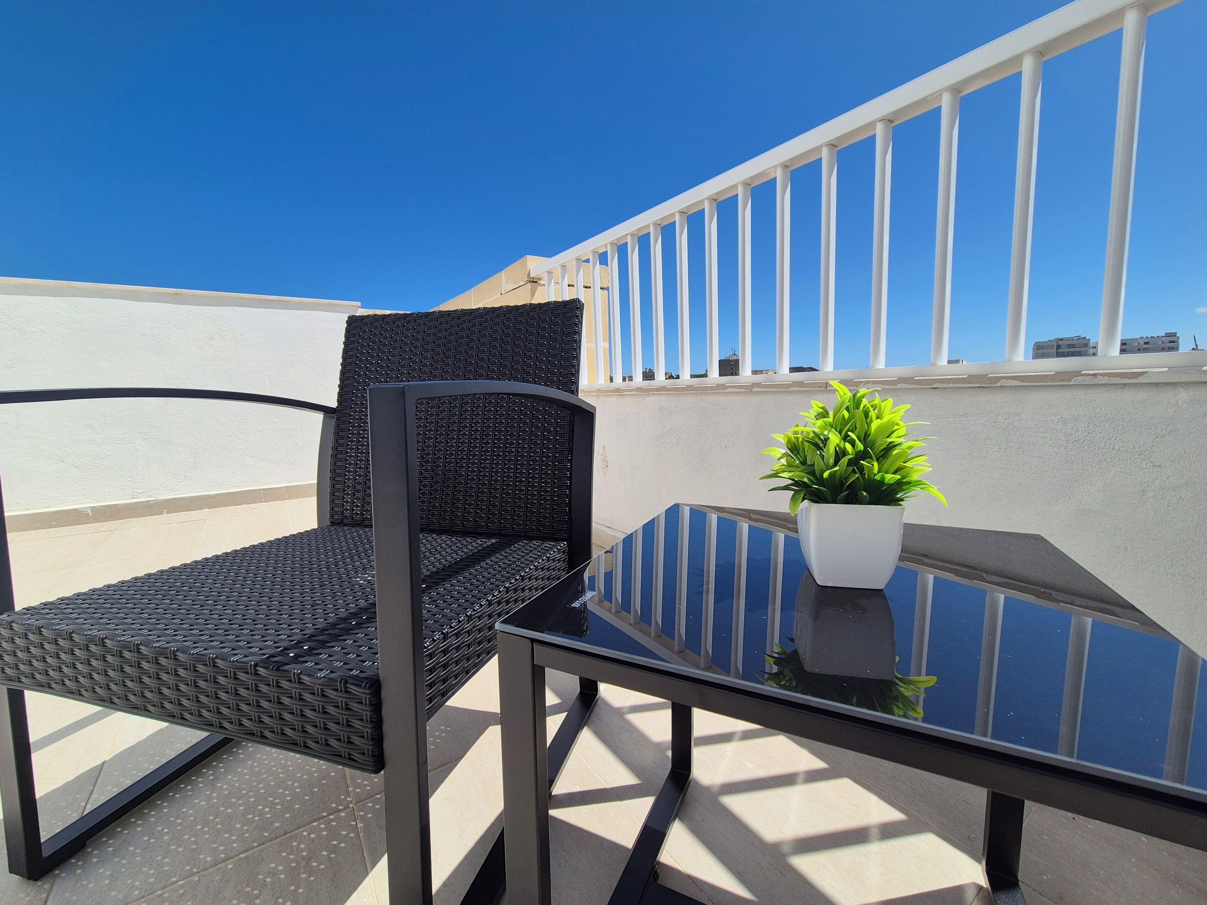 A balcony with a glass table, two wicker chairs, and a potted plant.