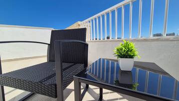 A balcony with a glass table, two wicker chairs, and a potted plant.