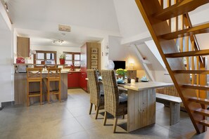 Eine moderne Küche mit Holzschränken, ein Essbereich mit Korbstühlen und eine sichtbare Treppe.