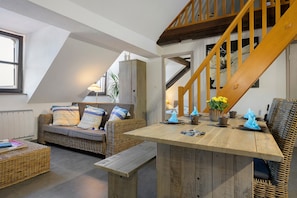 Ein gemütlicher Wohnbereich mit Holztisch, Korbmöbeln und einer Treppe.